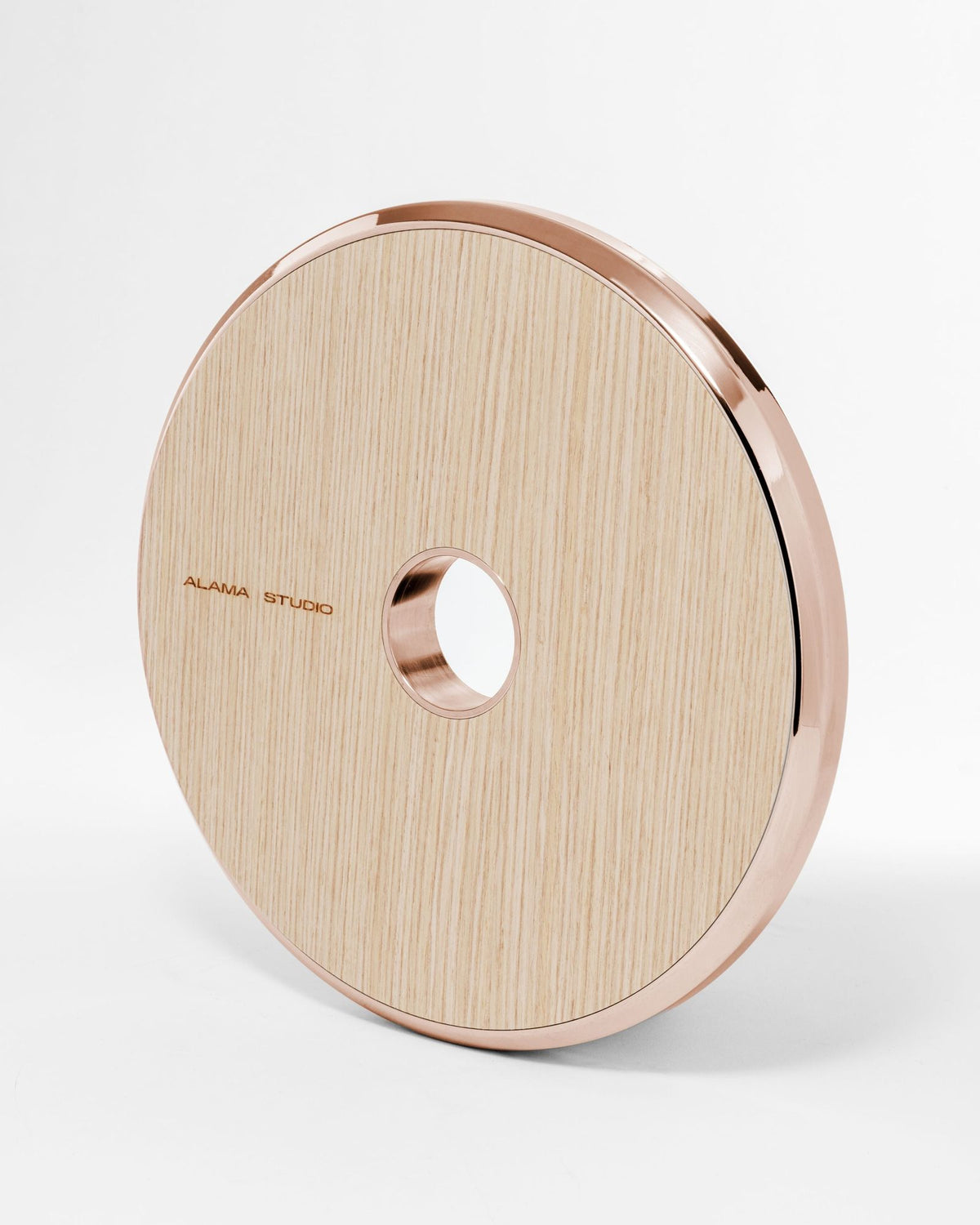 Alama Studio barbell weight: a disc faced in pale wood with a polished rose gold rim and centre ring, the Alama Studio name on its face, on a pale grey ground.