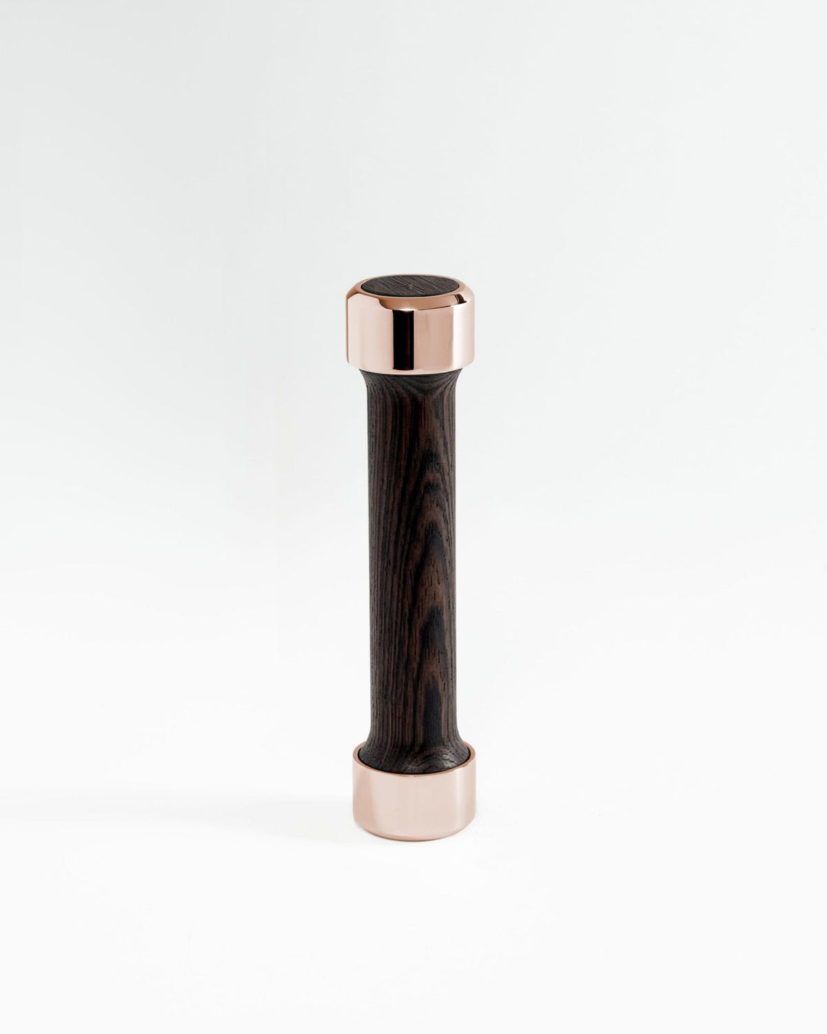 Alama Studio small weight standing upright: a slim dark wood handle between two polished rose gold ends, on a pale grey ground.