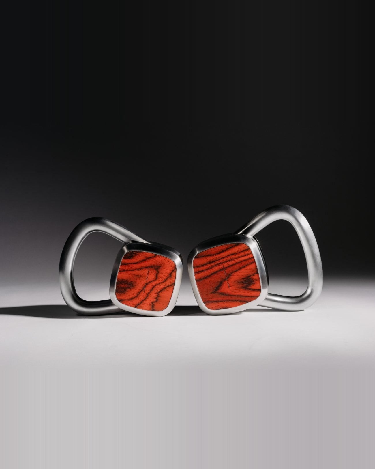 A sculptural pair of Alama weights in brushed steel and red wood, lit like design objects within a designed cabin interior.