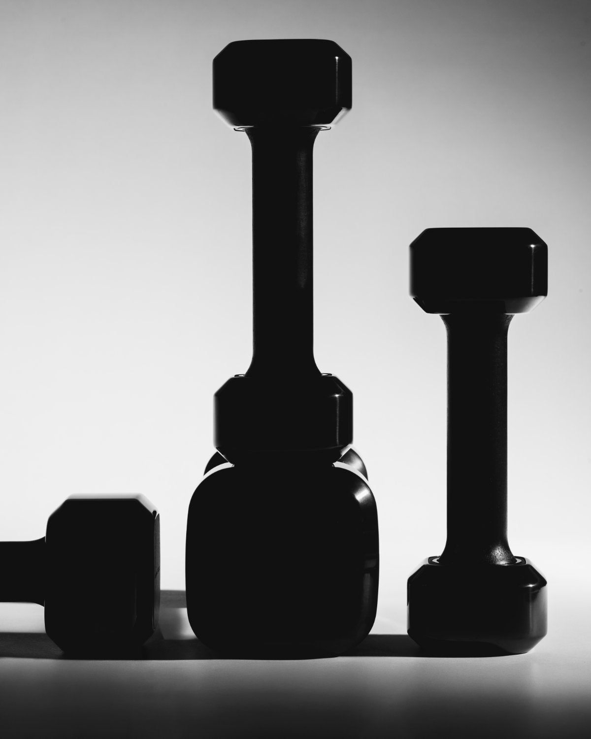 Three Alama dumbbells in graduated sizes, sculptural profiles lit on a pale background.