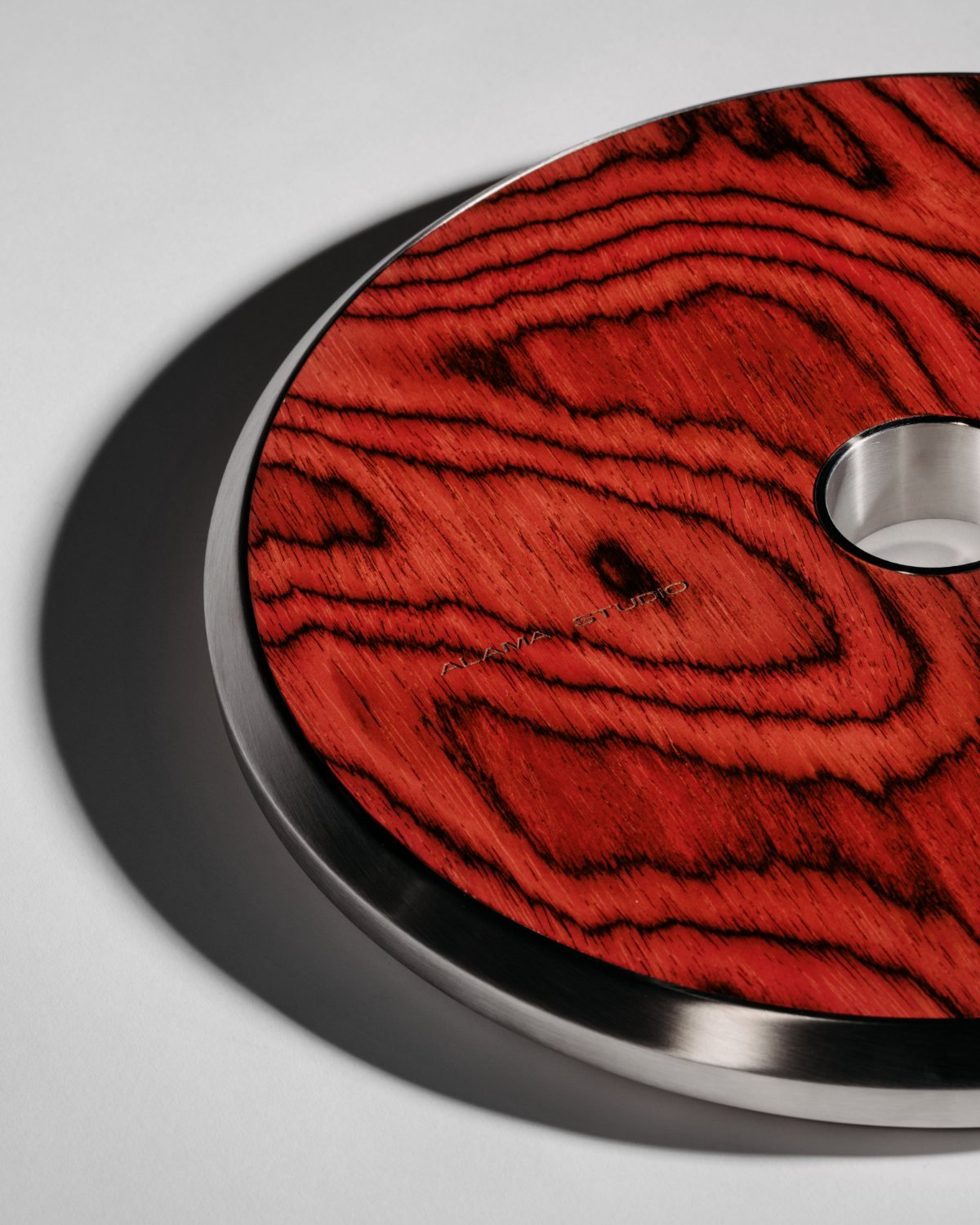 Macro of an Alama plate: marine-grade steel rim around a deep red ALPI wood face, engraved Alama Studio.